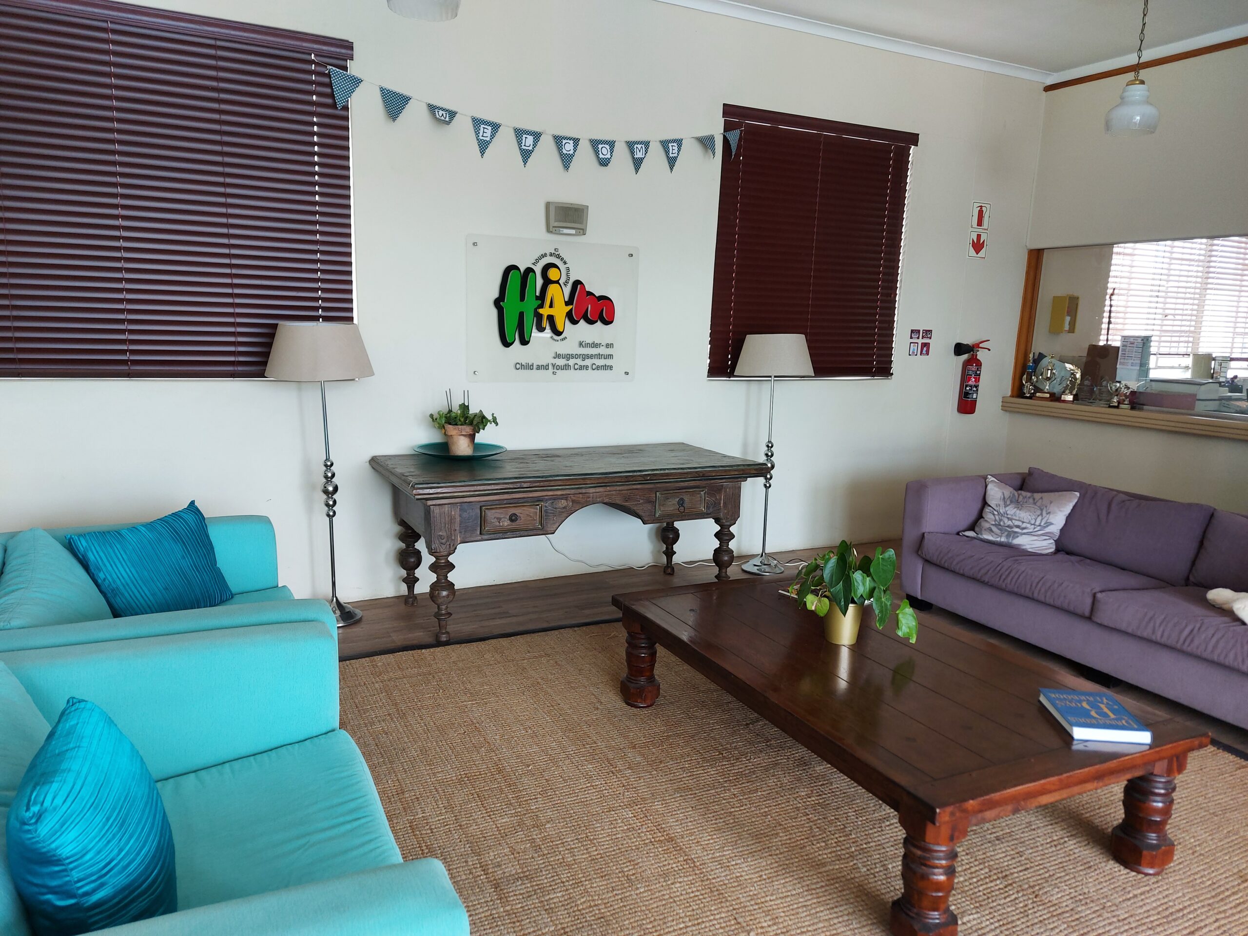 Lounge area featuring turquoise and purple sofas with a wooden coffee table and decorative plants.