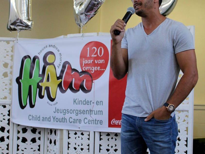 Man speaking into a microphone at a Child and Youth Care Centre event with balloons in the background.