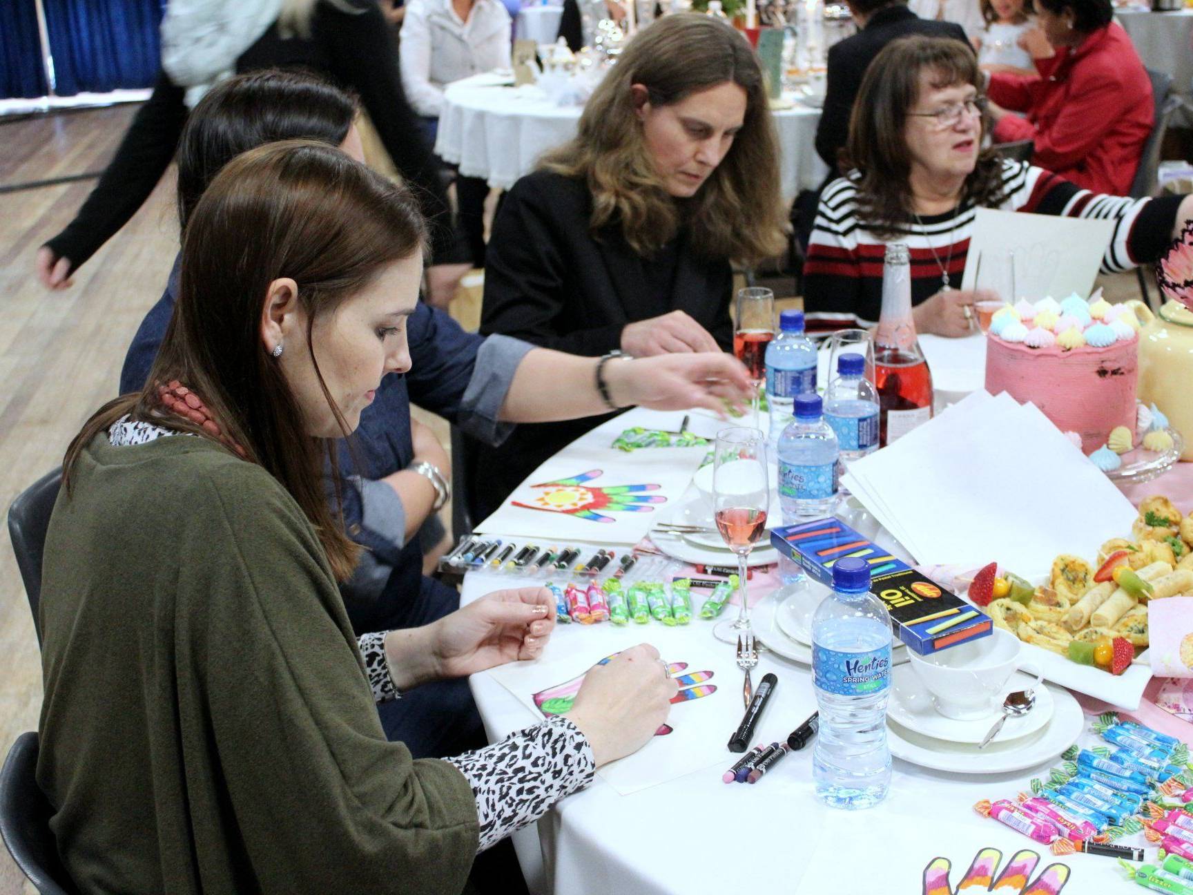 Women participating in a craft activity at a table with snacks and drinks.